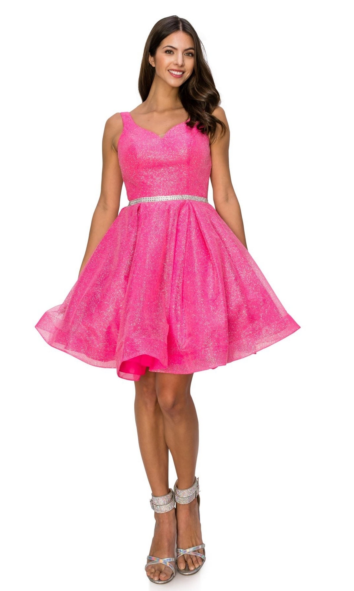 A woman stands smiling in the Short Glitter Princess Homecoming Dress 8047J—sleeveless, knee-length, bright pink with sparkling texture—paired with a silver belt and silver high-heeled sandals.